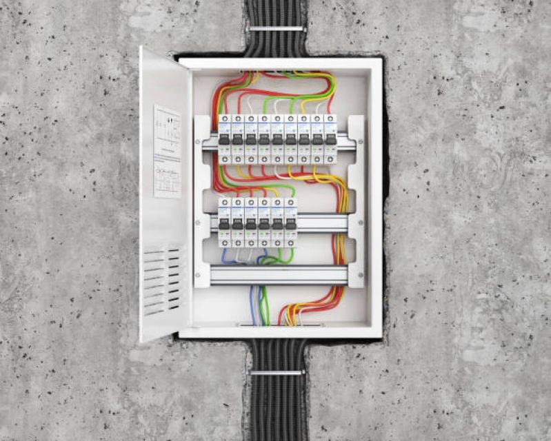 Open electrical junction box with multiple circuit breakers and colorful wiring against a concrete wall.