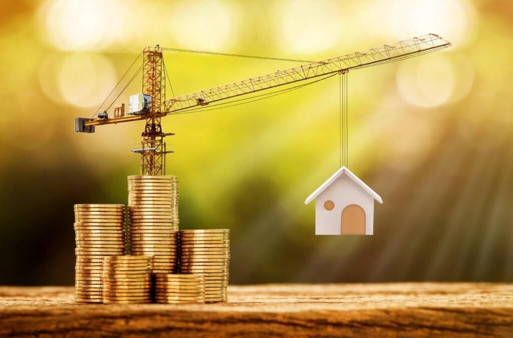 Crane lifting a small model house over stacks of gold coins against a blurred green background.