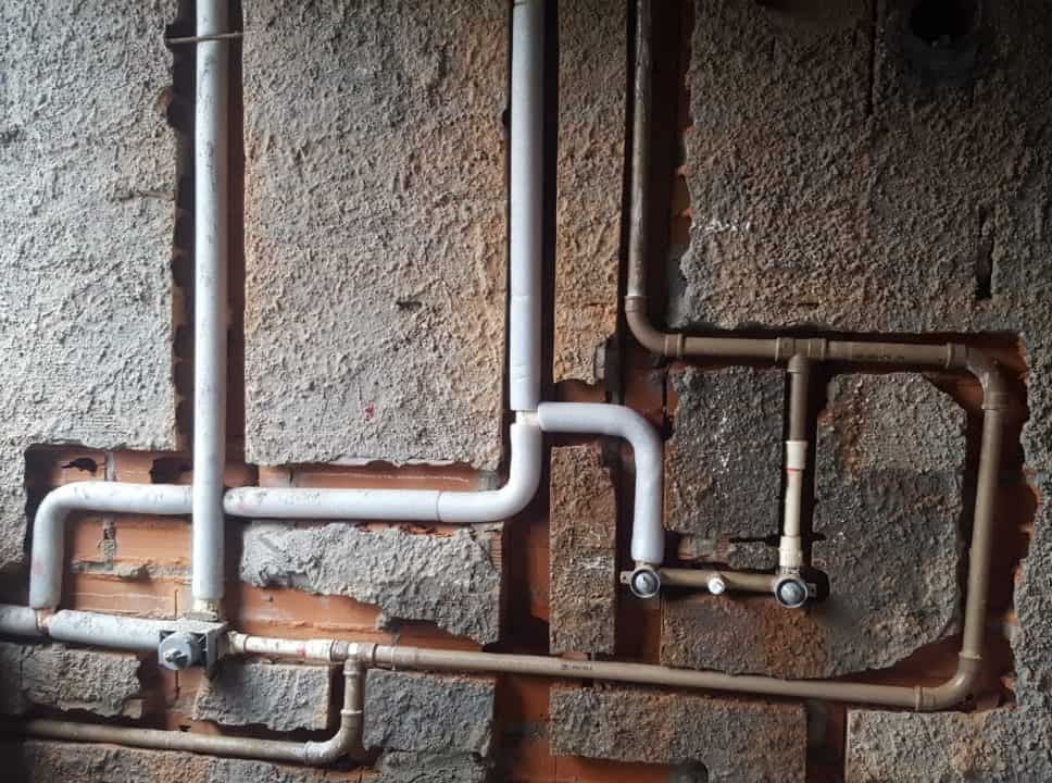 Exposed network of plumbing pipes on a textured wall.